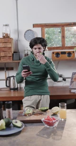 Vídeo Vertical Del Hombre Feliz Biracial Comiendo Sándwich Usando Smartphone — Vídeo de stock