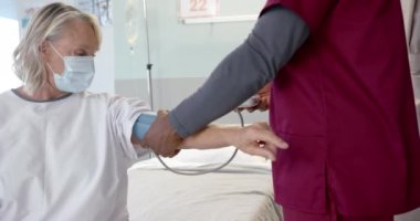 Afro-Amerikalı erkek doktor, hastanedeki beyaz kadın hastanın kan basıncını ölçüyor. Protez ve sağlık hizmetleri kavramı.