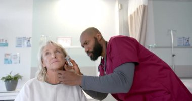 Ototoskoplu Afro-Amerikan erkek doktor. Hastanedeki beyaz kadın hastanın kulağını inceliyor. Protez ve sağlık hizmetleri kavramı.