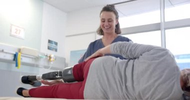 Caucasian female physiotherapist stretching prosthetic leg of female patient at rehab center. Prosthetics, physiotherapy rehabilitation and medical healthcare concept