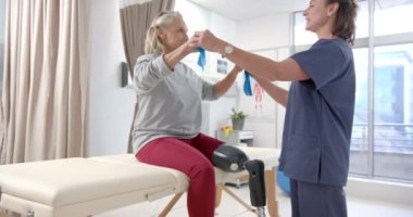 Caucasian female physiotherapist and female senior patient with prosthetic leg exercising. Prosthetics, physiotherapy rehabilitation and medical healthcare concept