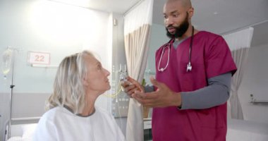 Ototoskoplu Afro-Amerikan erkek doktor. Hastanedeki beyaz kadın hastanın kulağını inceliyor. Protez ve sağlık hizmetleri kavramı.