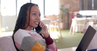 Mutlu Afro-Amerikan iş kadını ofis salonunda akıllı telefonuyla konuşuyor, ağır çekimde. İş, iş, iletişim ve günlük ofis, değiştirilmemiş.