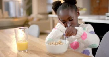 Afro-Amerikalı kız mısır gevreğini sütle yiyor, yavaş çekimde. Sağlıklı yaşam tarzı, çocukluk, yemek ve ev hayatı, değişmemiş..