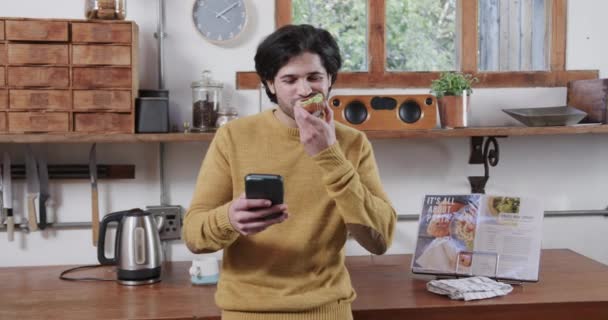 Hvit Mann Som Spiser Avokado Toast Bruker Smarttelefon Kjøkkenet Sakte – stockvideo