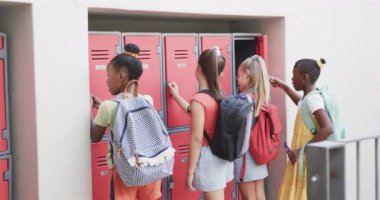 Okul çantaları takan ve ilkokuldaki dolaplarda konuşan mutlu liseli kızlar. Okul, eğitim ve eğitim, değiştirilmemiş..
