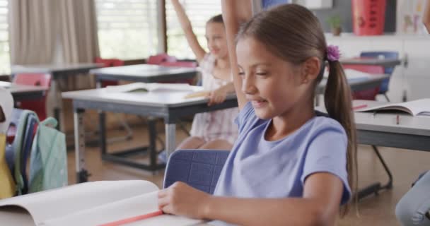 Onnellinen Monipuolinen Koulutytöt Pöydillä Nostaa Kätensä Luokkahuoneessa Peruskoulussa Koulu Opiskelu — kuvapankkivideo