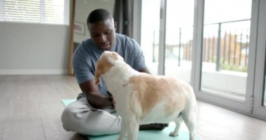 Afrika kökenli Amerikalı bir adam yoga minderinde oturuyor, evcil köpeğini evde okşuyor, ağır çekimde. Yaşam tarzı, kişisel bakım, evcil hayvanlar ve ev hayatı, değişmemiş..