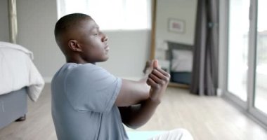 Afrika kökenli Amerikalı adam yoga yapıyor ve evde esneme hareketleri yapıyor, ağır çekimde. Yaşam tarzı, kişisel bakım, rahatlama ve ev hayatı, değişmemiş..