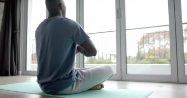 Afrika kökenli Amerikalı adam yoga yapıyor ve evde meditasyon yapıyor, ağır çekimde. Yaşam tarzı, kişisel bakım, rahatlama ve ev hayatı, değişmemiş..