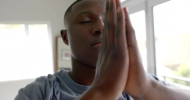 Afrika kökenli Amerikalı adam yoga yapıyor ve evde meditasyon yapıyor, ağır çekimde. Yaşam tarzı, kişisel bakım, rahatlama ve ev hayatı, değişmemiş..