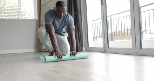 Afrikanischer Mann Der Hause Eine Yogamatte Auf Den Boden Legt — Stockvideo