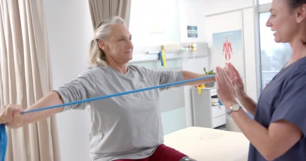 Caucasian Female Physiotherapist Helping Female Senior Patient Exercise Resistance Bands — Stockvideo