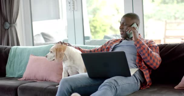 Χαρούμενος Αφροαμερικάνος Στο Smartphone Και Φορητό Υπολογιστή Στο Σπίτι Σκυλάκι — Αρχείο Βίντεο