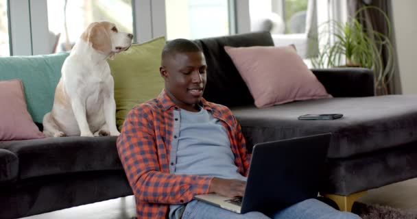 快乐的非洲裔美国人坐在地板上 在家里用笔记本电脑 带着他的宠物狗 慢动作 生活方式 宠物和家庭生活 — 图库视频影像