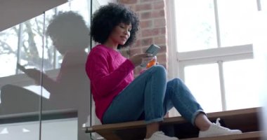 İki ırklı bir kadın çay içiyor ve evde akıllı telefon kullanıyor, ağır çekimde. Yaşam tarzı, iletişim ve aile hayatı, değişmedi..