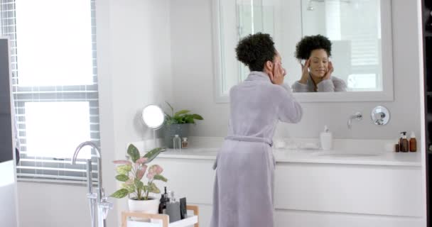 バスルームで鏡を見ているバスローブでハッピーな女性 ゆっくりとした動き ライフスタイル セルフケア 家庭生活 変わらない — ストック動画