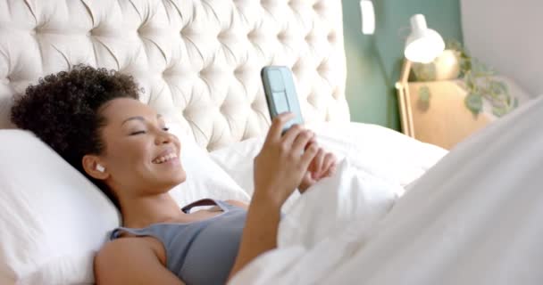 Heureuse Femme Biraciale Avec Des Écouteurs Couchés Dans Lit Utilisant — Video