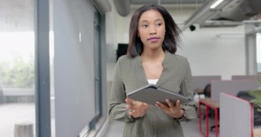 Ofiste yürürken dijital tablet kullanan Afrikalı Amerikalı iş kadını. İş, teknoloji ve ofis kavramı