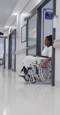 Hastane koridorunda tekerlekli sandalyedeki Afrikalı Amerikalı kadın hastanın dikey videosu, yavaş çekim. Sağlık hizmetleri, sağlık ve ilaç, değiştirilmemiş..