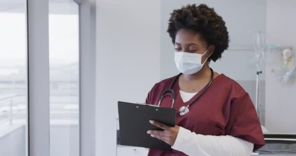 アフリカ系アメリカ人女性医師がフェイスマスクを着用し 病院の部屋に文書を保管し 動きが遅い メディカルサービス 変わらない — ストック動画