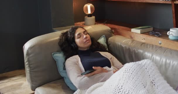 Biracial Γυναίκα Ξαπλωμένη Στον Καναπέ Κάτω Από Κουβέρτα Ακούγοντας Μουσική — Αρχείο Βίντεο