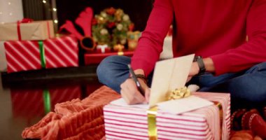 Çift ırklı bir adam, evde Noel kartı ile Noel tebriklerini yazıyor, ağır çekimde. Yaşam tarzı, Noel, kutlama, hediye ve ev hayatı, değişmemiş..