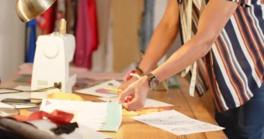 Çift ırklı erkek moda tasarımcısı stüdyoda masa başında duruyor, ağır çekimde. Moda, tasarım, yaratıcılık, giyim ve küçük işletmeler, değiştirilmemiş.