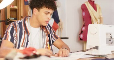 Çift ırklı erkek moda tasarımcısı tasarımı ve stüdyoda akıllı telefon kullanımı, yavaş çekim. Moda, tasarım, yaratıcılık, teknoloji, iletişim, giyim ve küçük işletmeler, değiştirilmemiş.