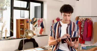 Çift ırklı erkek moda tasarımcısı stüdyoda bir tablet kullanıyor, ağır çekimde. Moda, tasarım, yaratıcılık, giyim, teknoloji, iletişim ve küçük işletmeler, değiştirilmemiş.