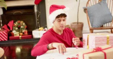 Çift ırklı bir adam Noel hediyesini dekoratif bir kağıda sarıyordu, ağır çekimde. Yaşam tarzı, Noel, kutlama, hediye ve ev hayatı, değişmemiş..