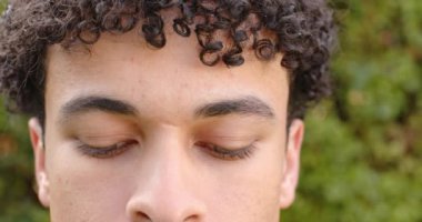 Çift ırklı bir adam yüzünü kapar ve dışarıdaki kameraya bakar, ağır çekimde. Erkeklik, doğa, kaplama ve açık hava, değiştirilmemiş.