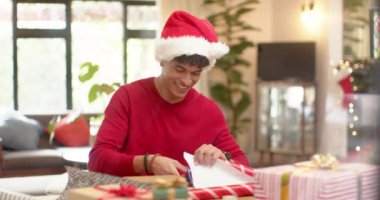 Çift ırklı bir adam Noel hediyesini dekoratif bir kağıda sarıyordu, ağır çekimde. Yaşam tarzı, Noel, kutlama, hediye ve ev hayatı, değişmemiş..