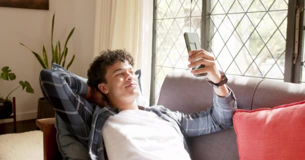 Biracial Pria Berbaring Sofa Dan Memegang Smartphone Rumah Gerakan Lambat — Stok Video