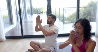 Çift ırklı çift evde yoga yapıyor ve yavaş çekimde meditasyon yapıyor. Yaşam tarzı, rahatlama ve ev hayatı, değişmemiş..