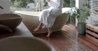 Küvette oturan, banyoda çay içen, ağır çekimde çift ırklı bir kadın. Yaşam tarzı, rahatlama, kişisel bakım ve ev hayatı, değişmemiş..