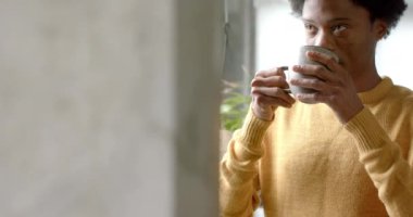 Afrika kökenli Amerikalı bir adam kahve içip pencereden dışarı bakıyor. Yavaş çekimde, fotokopi çekerek. Yaşam tarzı ve ev hayatı, değişmedi..