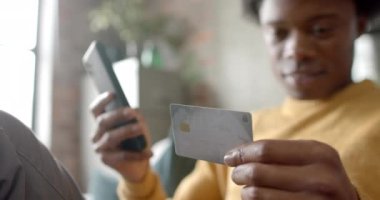 Mutlu Afro-Amerikan adam kanepeye oturmuş akıllı telefonu kullanarak evde online alışveriş yapıyor, ağır çekimde. Yaşam tarzı, iletişim, alışveriş ve ev hayatı, değişmedi..