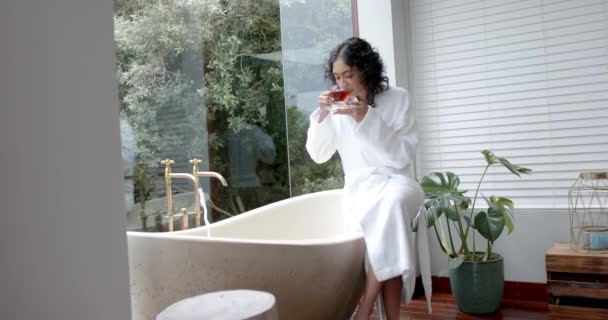 Biracial Woman Wearing Bathrobe Sitting Bathtub Drinking Tea Bathroom Home — Stock Video