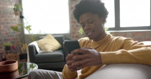 Szczęśliwy Afrykański Amerykanin Siedzący Kanapie Korzystający Smartfona Domu Zwolnionym Tempie — Wideo stockowe