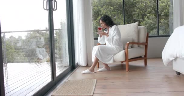 Biracial Γυναίκα Φορώντας Μπουρνούζι Πίνοντας Τσάι Και Κοιτάζοντας Μέσα Από — Αρχείο Βίντεο