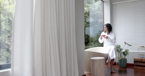 Mujer Biracial Con Albornoz Sentada Bañera Bebiendo Casa Cámara Lenta — Vídeos de Stock