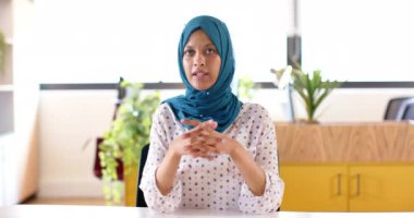 Çift ırklı, tesettürlü iş kadını ofiste video görüşmesi yapıyor, yavaş çekim. Günlük ofis, iş, iletişim ve iş, değiştirilmemiş.