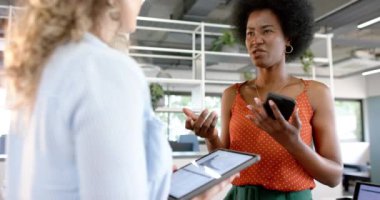 Ofiste tablet ve akıllı telefon kullanan çeşitli yaratıcı bayan meslektaşlar, yavaş çekim. Günlük ofis, iş, takım çalışması, iletişim ve çalışma, değiştirilmemiş.