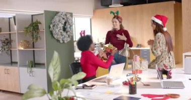 Mutlu çeşitli yaratıcı bayan meslektaşlar ofiste Noel hediyeleri veriyorlar, ağır çekimde. Günlük ofis, iş, Noel, gelenek, kutlama ve çalışma, değiştirilmemiş.