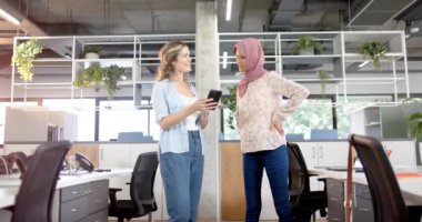 Ofisteki akıllı telefonu kullanarak tartışan mutlu yaratıcı bayan meslektaşlar, yavaş çekim. Günlük ofis, iş, takım çalışması, iletişim ve çalışma, değiştirilmemiş.