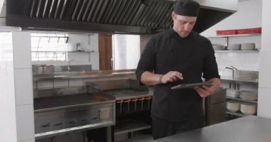 Kafkas erkek aşçı mutfakta tablet kullanıyor, ağır çekimde. Teknoloji, iletişim, yemek pişirme, meslek, yemek, eğitim, öğretim, restoran ve yemek servisi, değiştirilmemiş.