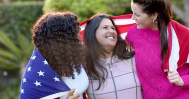 Güneşli bahçede sırtında bayrak olan üç farklı kadın arkadaş. Kutlama, dostluk, vatanseverlik, Amerikan kültürü ve geleneği değişmedi..