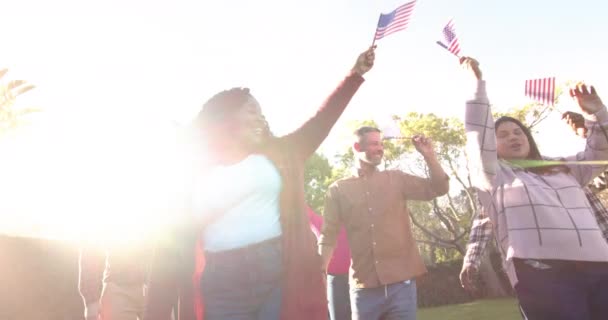 ハッピーな多様な男性と女性の友人が日当たりの良い庭で旗で踊っています 愛国心 アメリカの文化と伝統は変わらない — ストック動画