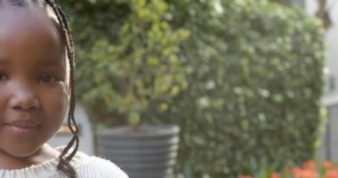 Saçları örgülü, güneşli bahçede gülümseyen, fotokopi çeken, ağır çekim Afrikalı Amerikalı bir kızın portresi. Çocukluk, boş zaman, refah ve yaşam tarzı, değişmemiş..